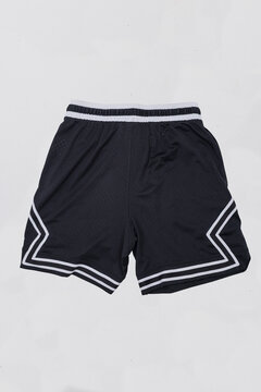 Flat lay back view of black athletic mesh basketball shorts with white geometric stripe details and an elastic waistband, isolated on a light background. Ideal for product mockup.