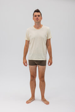 Full-body portrait of a young athletic man standing barefoot in a plain beige t-shirt and brown boxer briefs isolated on a white background. Perfect for apparel mockup and underwear catalog.