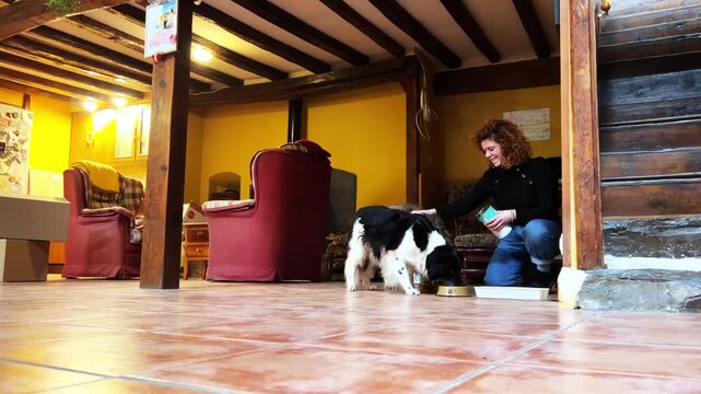 Woman petting her dog while it eats from a bowl in a rustic country house home