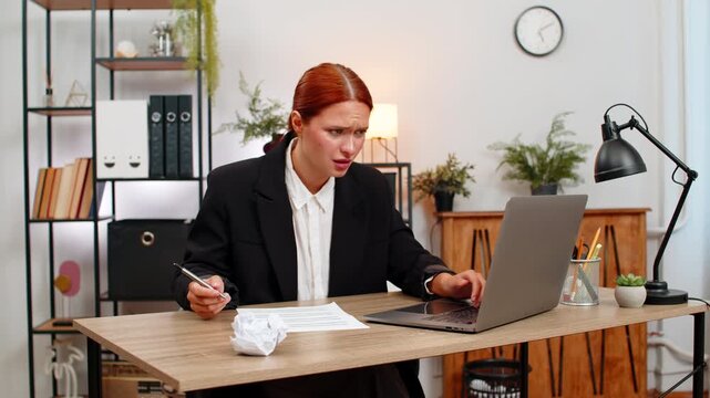 Young businesswoman at home office spots big report mismatch on laptop and angrily crushes paper fearing audit. Freelancer girl at table recalculates sums quickly aiming to correct data and avoid loss