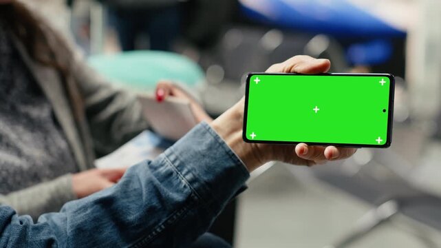 Older couple holds an isolated smartphone mockup in the airport lounge while planning a vacation itinerary, highlighting active retirement, unconventional lifestyle and green screen use.