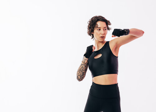 Woman in black sportswear wearing gloves and practicing shadow punches over a white backdrop