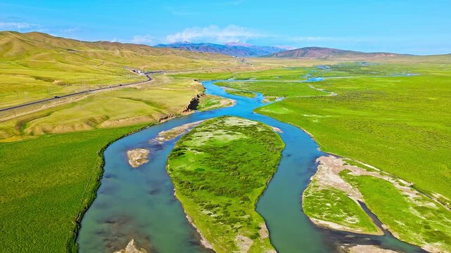 Aerial view of a meandering river flowing through a lush green valley under a blue sky in Xinjiang, China