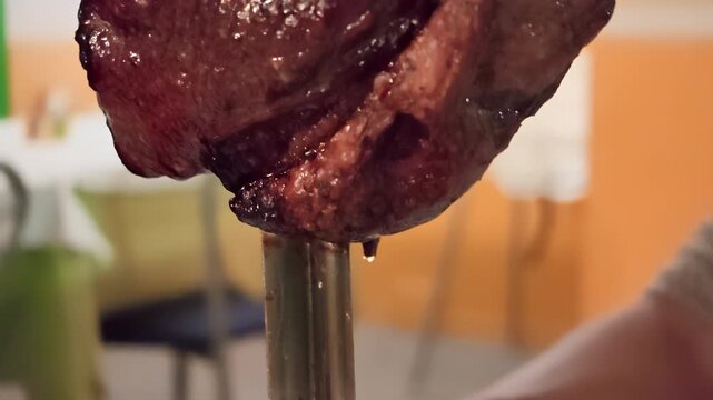 Closeup cutting juicy picanha roast beef from a rotating skewer at a traditional Brazilian steakhouse, preparing slices of grilled meat for serving at a churrascaria buffet. Romantic night dinner