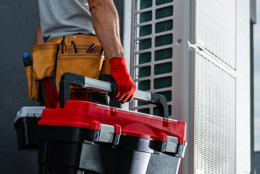 HVAC technician carrying toolboxes beside an outdoor unit