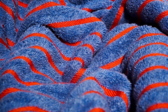 A close-up shot of a textured blue towel, with orange strips showcasing its fluffy and soft fabric loops. Blue towel with red striped as background, summer resort concept banner. Pool adv wool texture