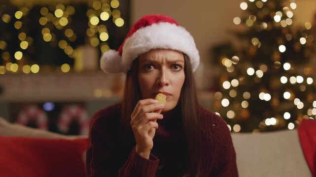 Surprised woman in Santa hat reacting to something and eating chips