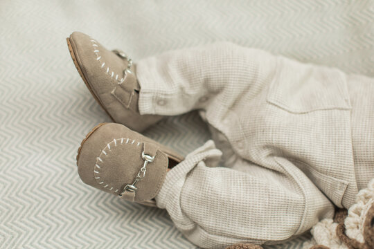 Newborn Baby Boy feet in adorable little light brown shoes in a cute little knitted outfit on a blanket
