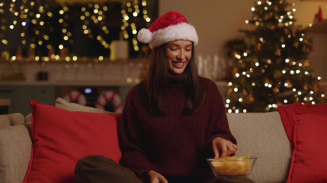 Woman in Santa hat relaxing on sofa with remote control and chips