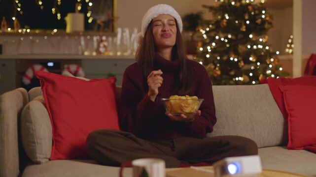 Woman in Santa hat eating chips while enjoying movie at home, 4K