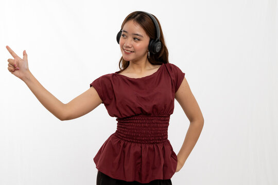 Young Woman Wearing Headphones Pointing Playfully While Standing Against a White Background