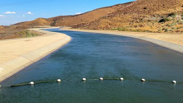 Pan-up of the California Aqueduct from a closeup of the water to the vista of desert and mountains beyond. Near Palmdale, this major canal is cut into the mountains above the Antelope Valley. 