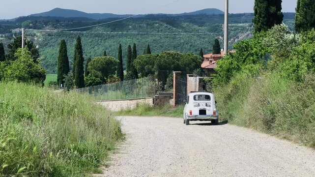 Classic oldtimer car driving through scenic rural Tuscany countryside road
