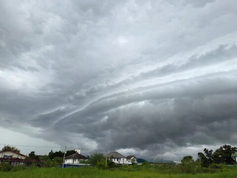 Approaching Storm: Dramatic, swirling grey storm clouds gather ominously over a rural landscape, hinting at an imminent downpour and casting a dramatic atmosphere over the scene.
