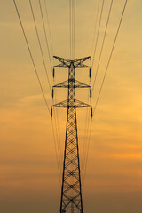 Obraz premium Symmetrical high-voltage electricity transmission tower silhouette against a golden sunset sky