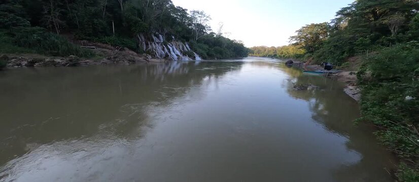 FPV drone flight over turquoise tropical waterfall in jungle, limestone canyon with crystal clear water and lush vegetation, cinematic aerial footage of pristine nature