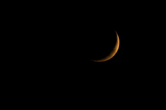 Golden crescent moon shining brightly in the pitch black night sky.A stunning atmospheric photograph of a slender, 