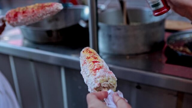 Woman's hand sprinkling chili powder on Mexican elote street food
