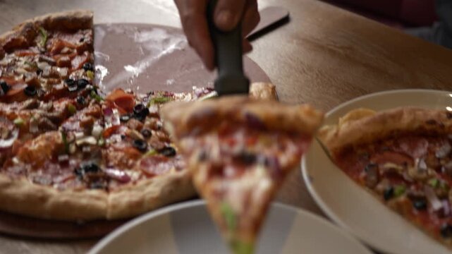Hand lifts a slice of pizza from a wooden board, placing it onto a white plate, showcasing a delicious array of toppings in a warm dining atmosphere