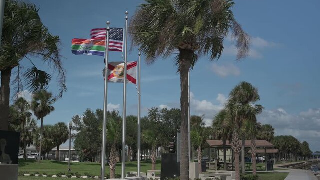 American, Florida and rainbow flags flutter above a manicured park with palm trees and a bright blue skye. St. Petersburg, FL evoking civic pride, diversity, warm weather and a relaxed Florida outdoor