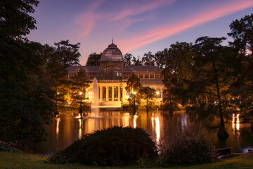Obraz premium Magical sunset at Palacio de Cristal (Glass Palace) in El Retiro Park, Madrid, with colorful clouds reflecting in the lake