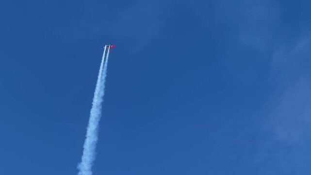 Stunt Plane Performing Aerobatic Maneuvers with Smoke Trails in Blue Sky