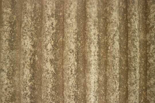 Close-up shot of an old weathered corrugated roof surface, showing textured patterns, earthy tones, and signs of decay