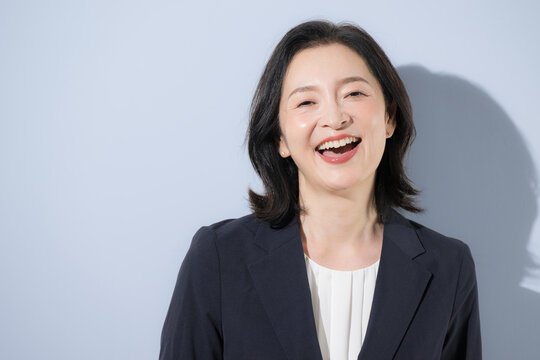 [水色背景]笑顔の日本人ミドル女性、スーツ姿で明るく前向きな50代の女性ビジネスパーソンのクローズアップ