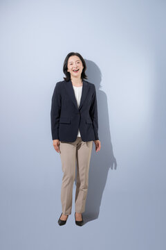 [水色背景]笑顔で立つ日本人ミドル女性、スーツ姿で明るく前向きな50代の女性ビジネスパーソンの全身