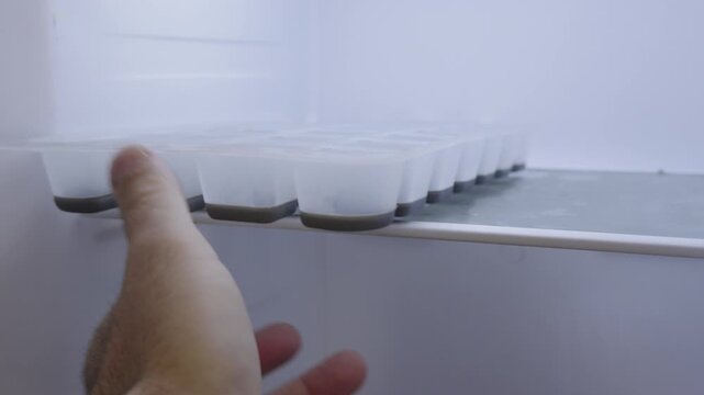 Man opens a freezer and discovers an empty ice cube tray. He looks inside, realizes there is no ice, and puts the tray back. Everyday household routine and relatable kitchen moment.