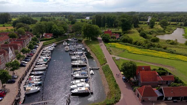 Wide horizontal aerial drone video of historic harbor marina, yachts, traditional windmill, red roof houses, and countryside moat in Veere, Zeeland, Netherlands on sunny afternoon