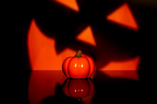 Halloween pumpkin with a giant spooky face shadow and reflection on a black background.