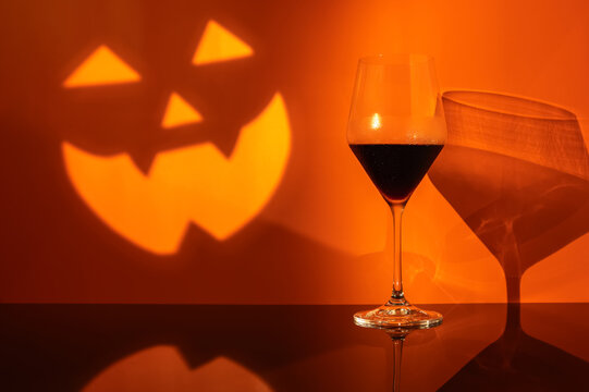 Halloween red wine glass against an orange wall featuring a jack o lantern face shadow.