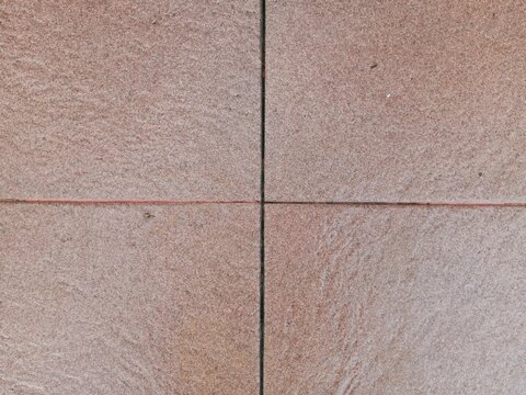 Top view of a neat cross joint intersecting four textured brown stone floor tiles. A simple, clean architectural background and geometric pattern