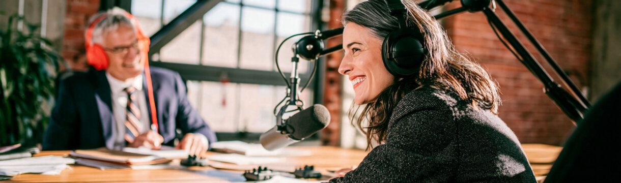 Podcast Interview Session: Two professionals, one female host with headphones and microphone and one male guest in suit, engage in a dynamic podcast interview, bathed in warm studio light.