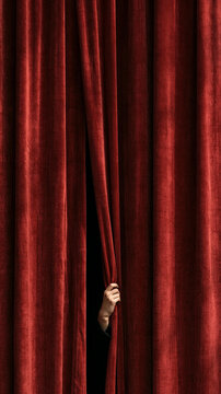 The Unveiling Moment: A mysterious hand gently parts a rich, velvet red curtain, inviting a sense of anticipation and curiosity as the stage awaits its grand reveal.