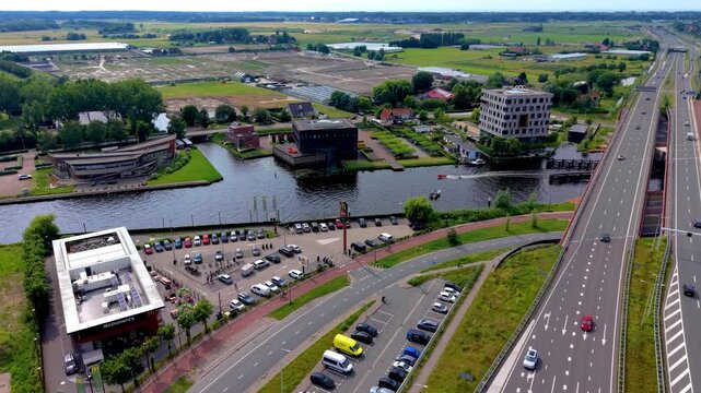 Wide horizontal aerial drone video of multi-lane highway overpass, canal waterway, McDonald's restaurant, office buildings, parking lots, and polder landscape in Leiden, South Holland, Netherlands