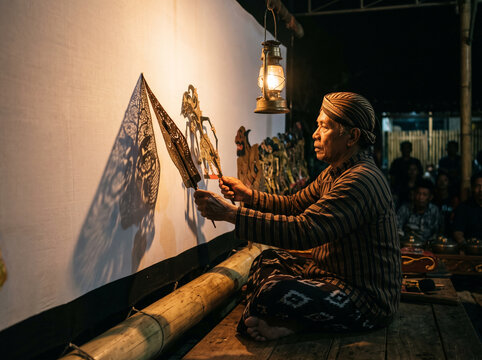 Cultural Stage Photography of Indonesian Dalang Performing Wayang Kulit Shadow Puppet Show Behind Illuminated Screen in Warm Brown and Off White for Cultural Heritage Banners