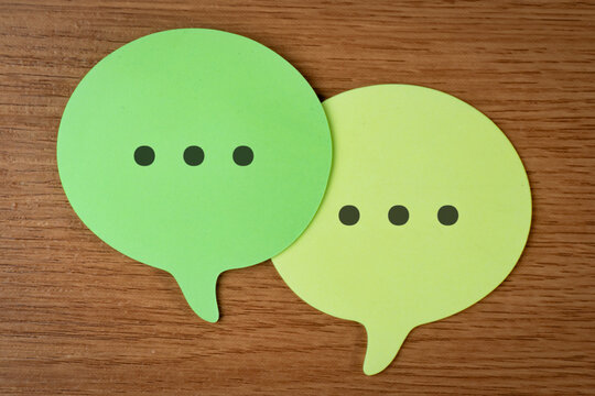 Two speech bubble with ellipsis typing indicators overlapping on a wooden desk. Online messaging, customer service feedback, social media communication, and live chat support concept.