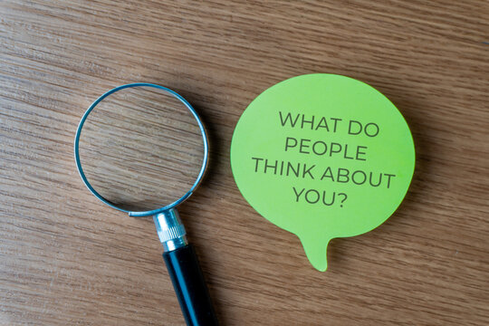 Magnifying glass and a speech bubble with text WHAT DO PEOPLE THINK ABOUT YOU? on a wooden desk. Social anxiety, public perception, brand reputation concept.