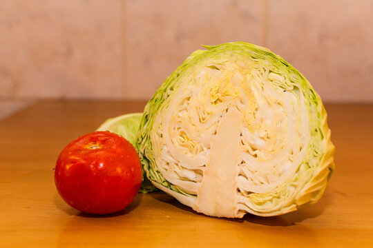 Composici&oacute;n de medio repollo verde texturizado y un tomate rojo fresco con gotas de agua sobre una mesa de madera. Bodeg&oacute;n de vegetales saludables.