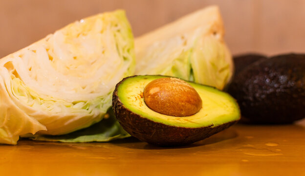 Medio aguacate con carozo en primer plano, con trozos borrosos de col verde fresca en el fondo desenfocado.