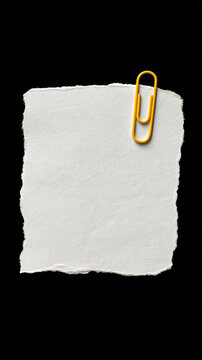 Torn Note with Gold Paperclip: A textured, torn piece of white paper, seemingly a memo or reminder, is held by a shiny gold paperclip, isolated on a stark black background.