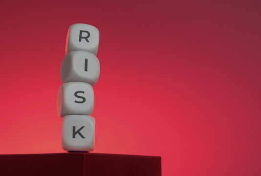 White dice with the word RISK precariously balanced on a dark edge against a red background. Risk management, business vulnerability, strategy failure, financial volatility, market disruption concept.