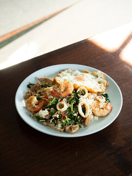 Pad Kaprao, Thai stir-fried holy basil, garlic, chili pepper with prawn, squid, chicken and minced pork, served with steamed rice and fried egg