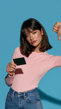 Disappointment in Consumer Choice: A young woman holds a blank card and gives a thumbs down, expressing dissatisfaction with a product or service.