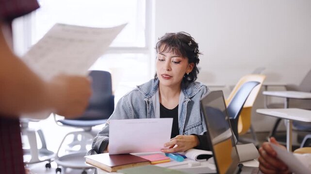 Female university student reviews a worksheet, listens to a classmate and writes notes during a collaborative Latino college study session