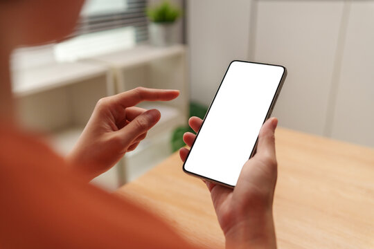 Woman holding smartphone with a blank white screen while tapping at home, representing mobile browsing, app mockup, digital communication, touchscreen technology and online lifestyle.
