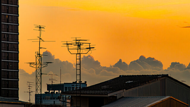Silhouette of Rooftop TV Antennas Against Vivid Orange Sunset Sky
