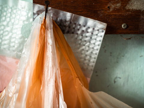 Torn Orange Plastic Bag Hanging from Nail with Ants on Weathered Wall